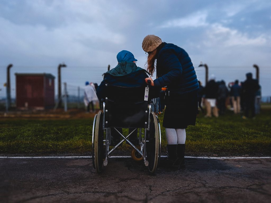 Frau, die in der Nähe einer Person im Rollstuhl in der Nähe einer grünen Wiese steht.